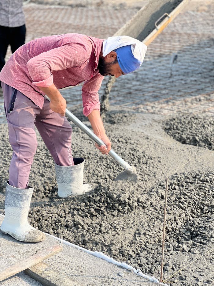 services-02 Worker in a pink shirt spreading concrete on a construction site with a shovel.